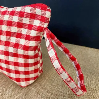 Vista laterale della pochette in cotone a quadretti rossi con manico in tessuto e logo cucito